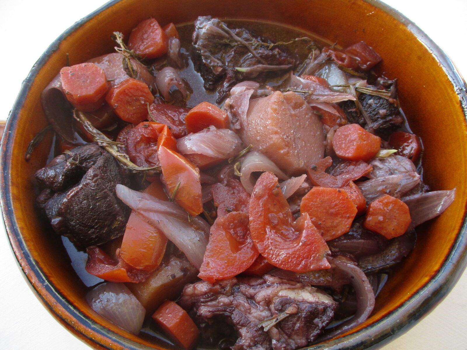 A glazed earthenware pot of beef daube with braised meat, sliced carrots, onions and pieces of tomato in a dark wine sauce