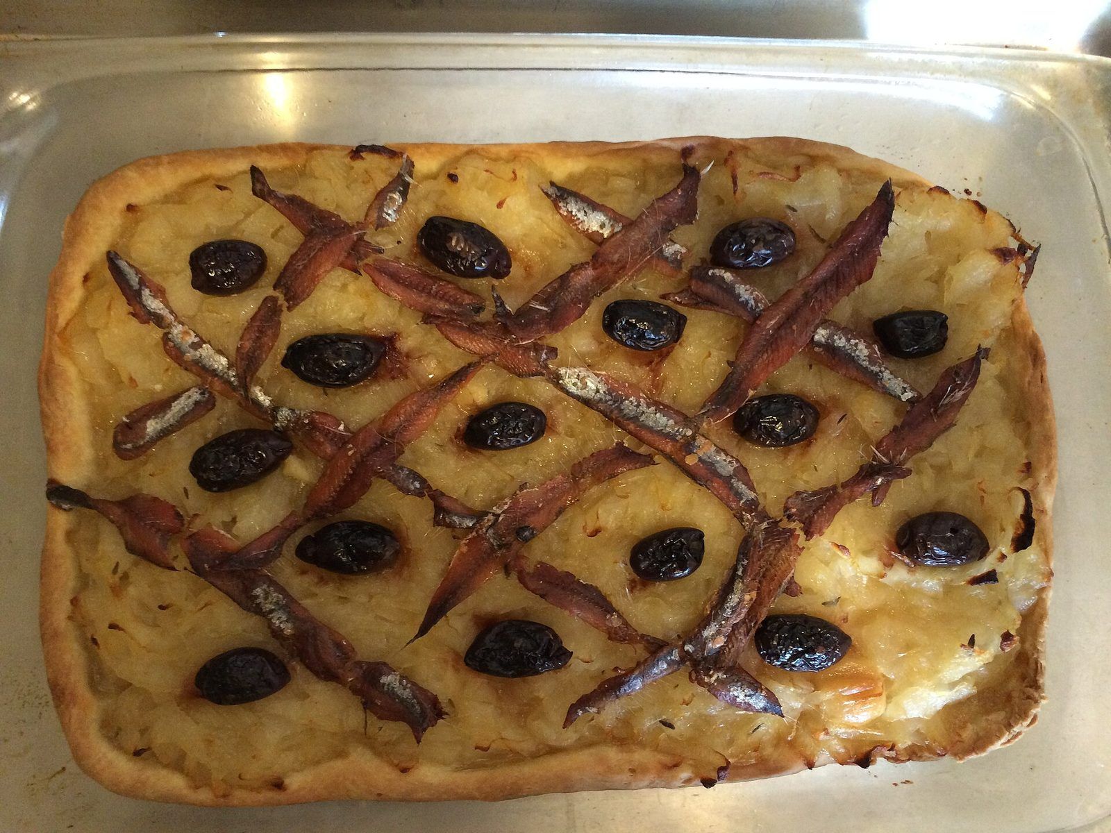 Pissaladière dans son plat, oignons fondants sous un quadrillage d'anchois et d'olives noires