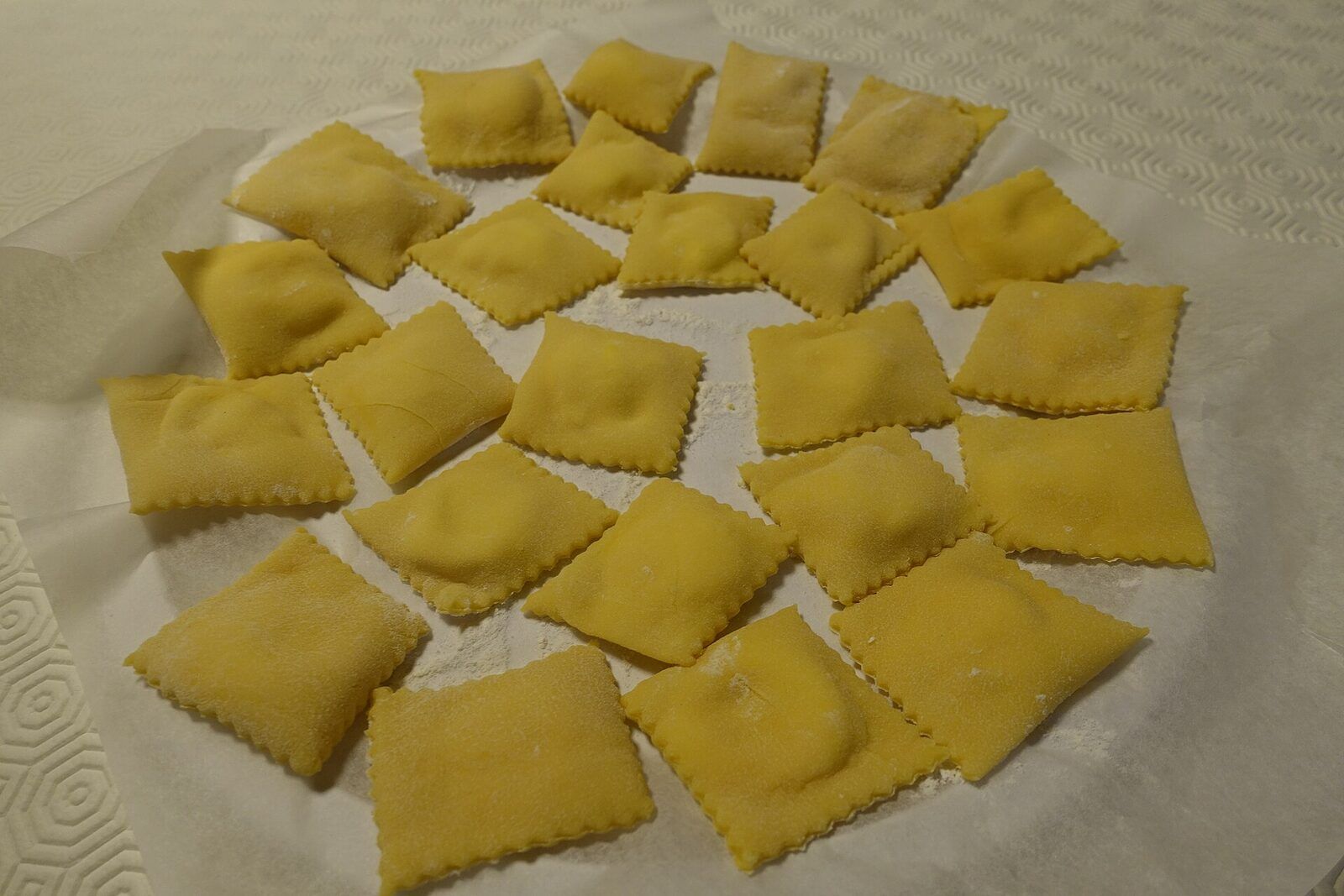Freshly cut square ravioli with fluted edges, dusted with flour and laid out on baking paper before cooking
