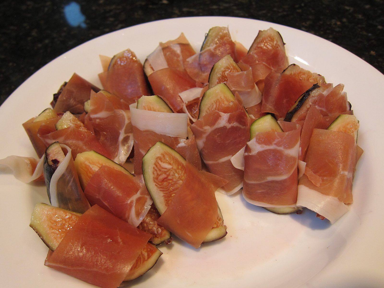 Quartiers de figues fraîches enroulés dans de fines tranches de jambon cru, sur une assiette blanche