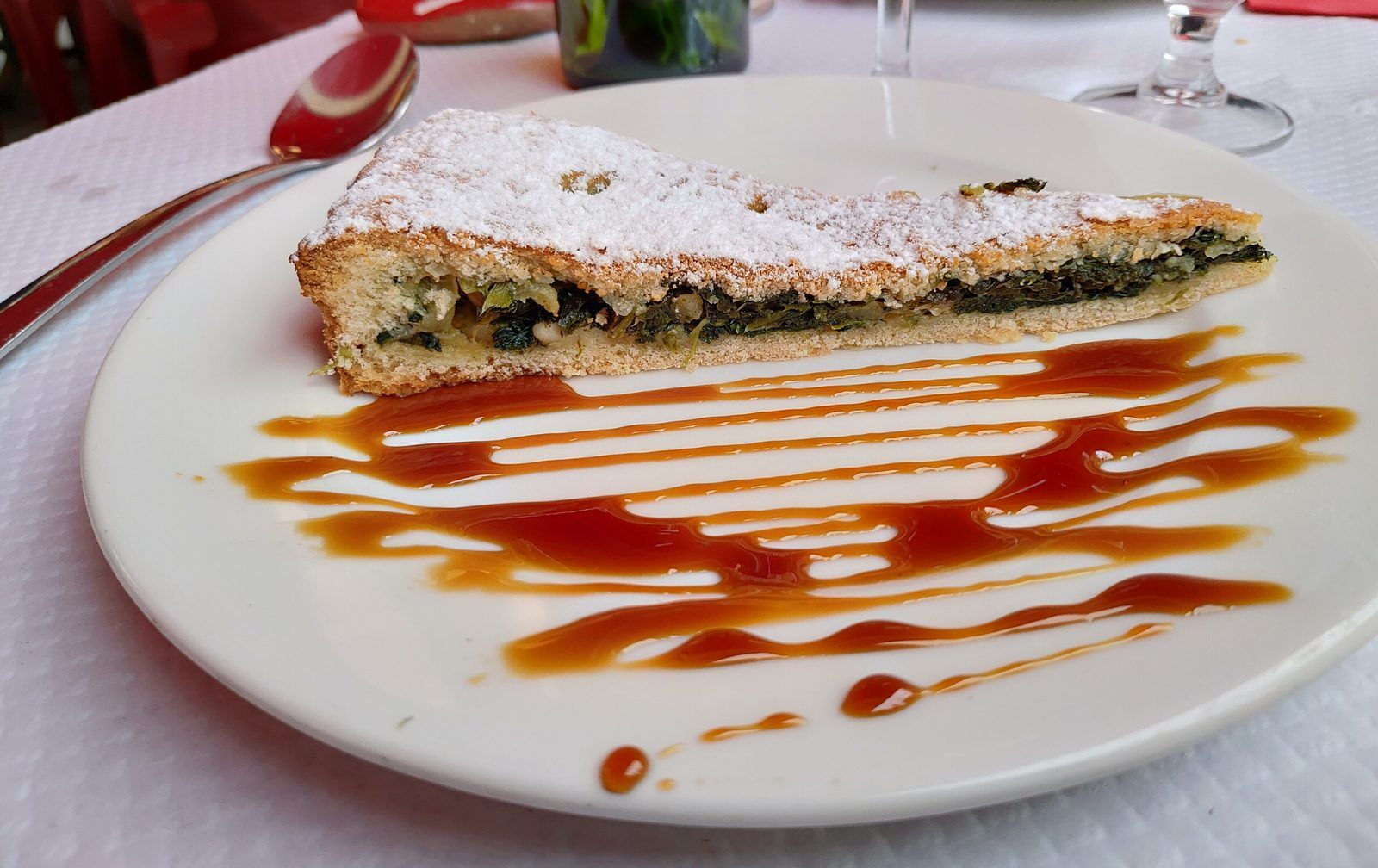 Part de tourte de blettes sucrée aux pignons, saupoudrée de sucre glace, servie avec un filet de caramel